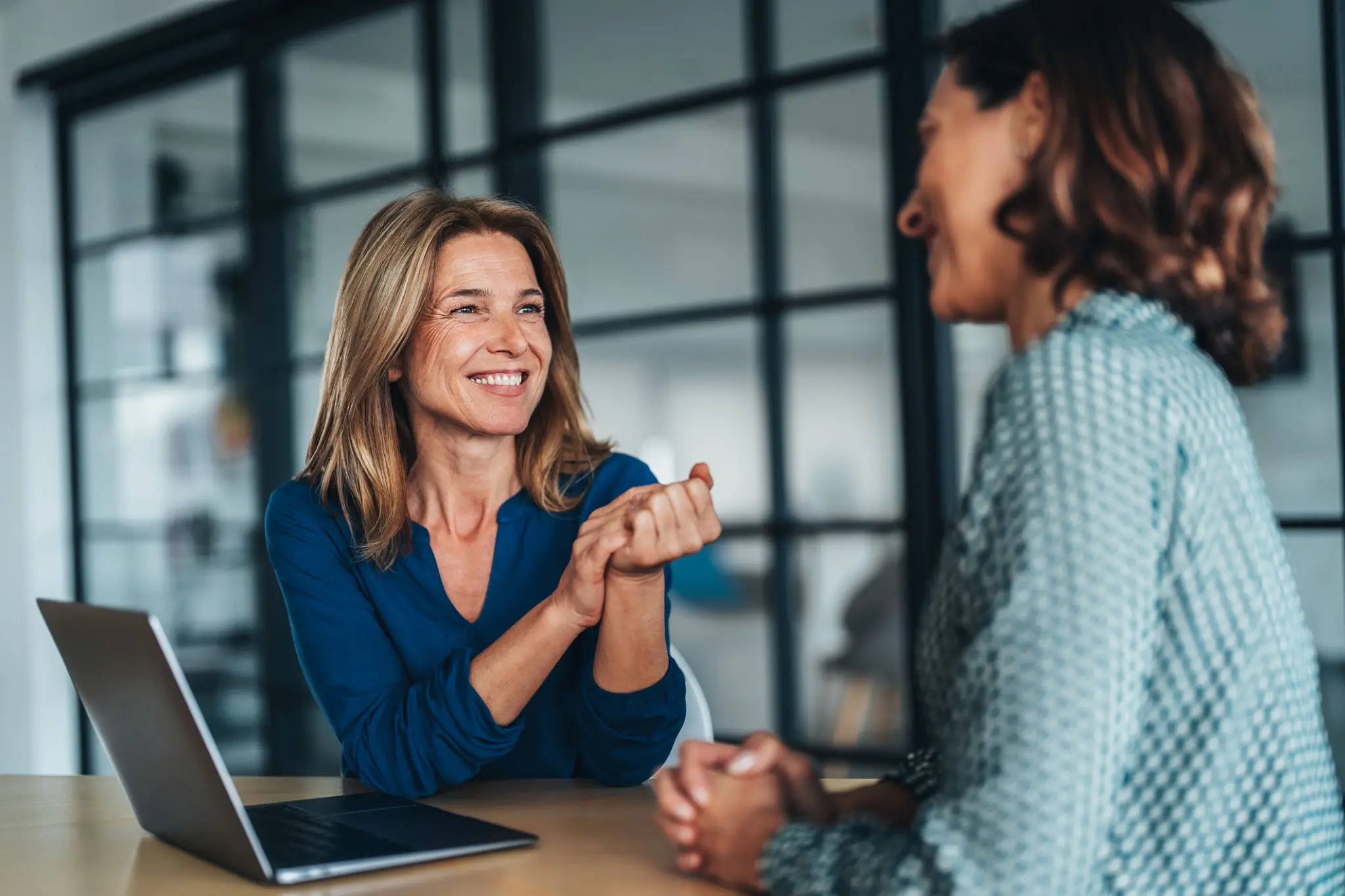 Two colleagues sharing a joyful conversation in a modern office.