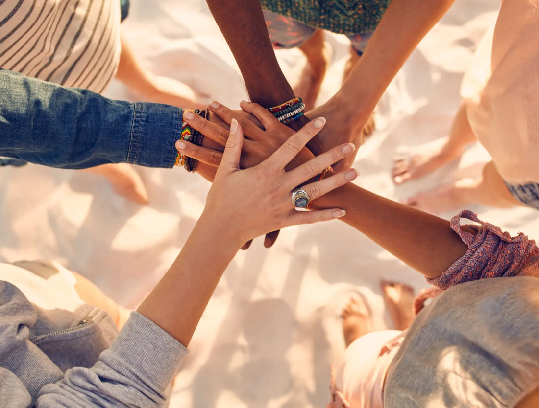 A group of friends stacking hands in unity on a sunny day.