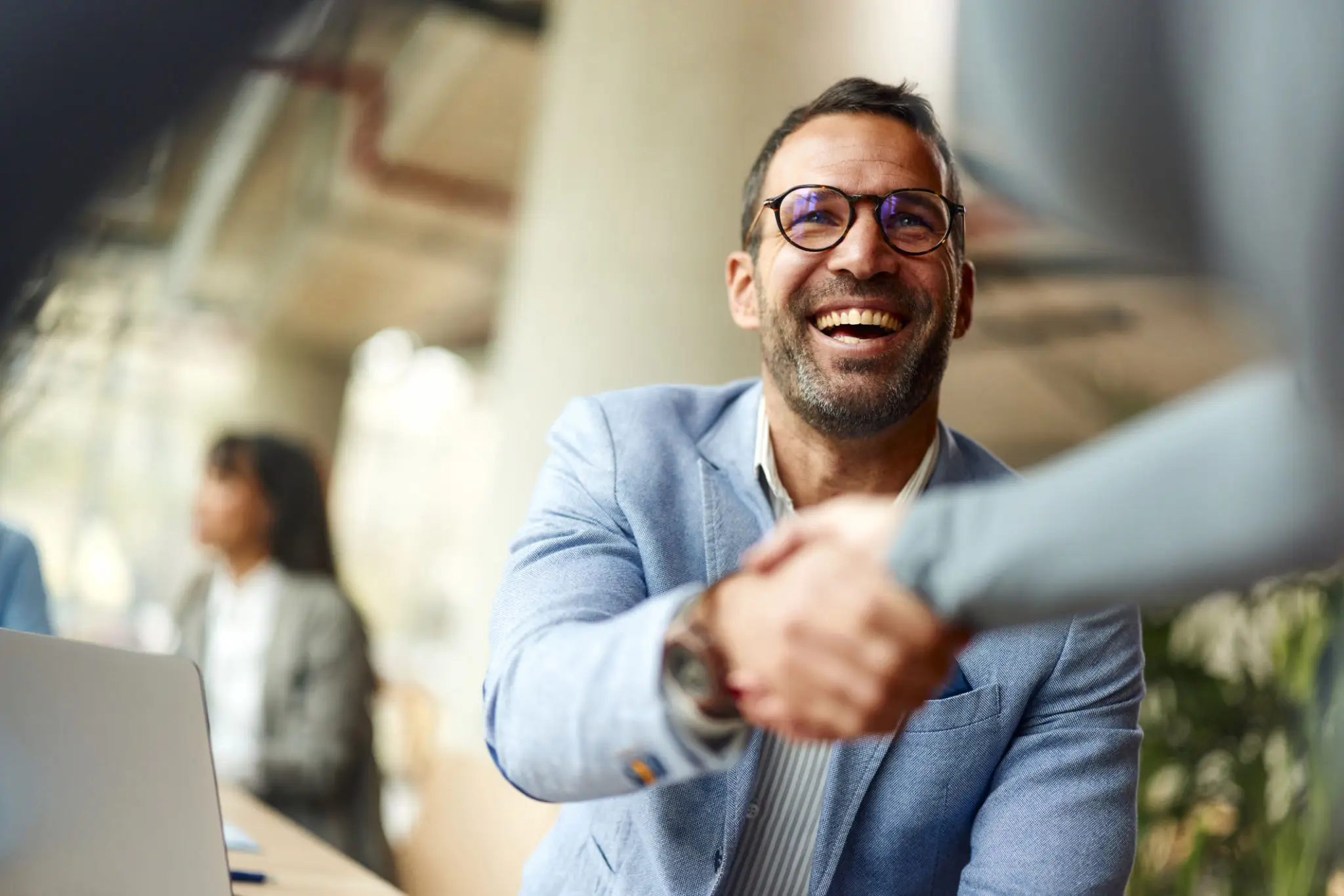 Smiling man in glasses shaking hands in a professional setting.