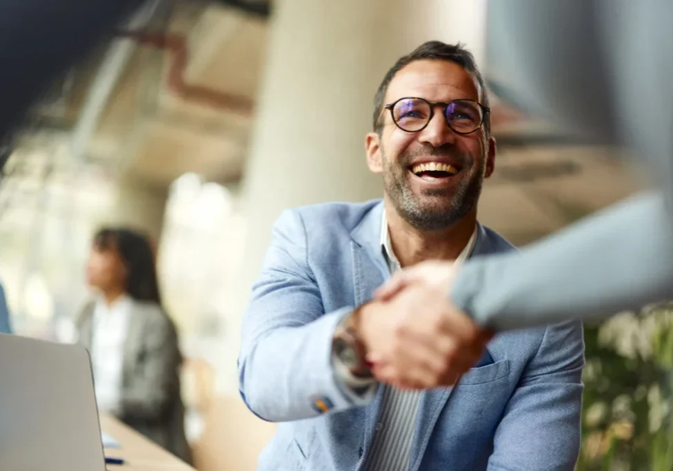 Smiling man in glasses shaking hands in a professional setting.